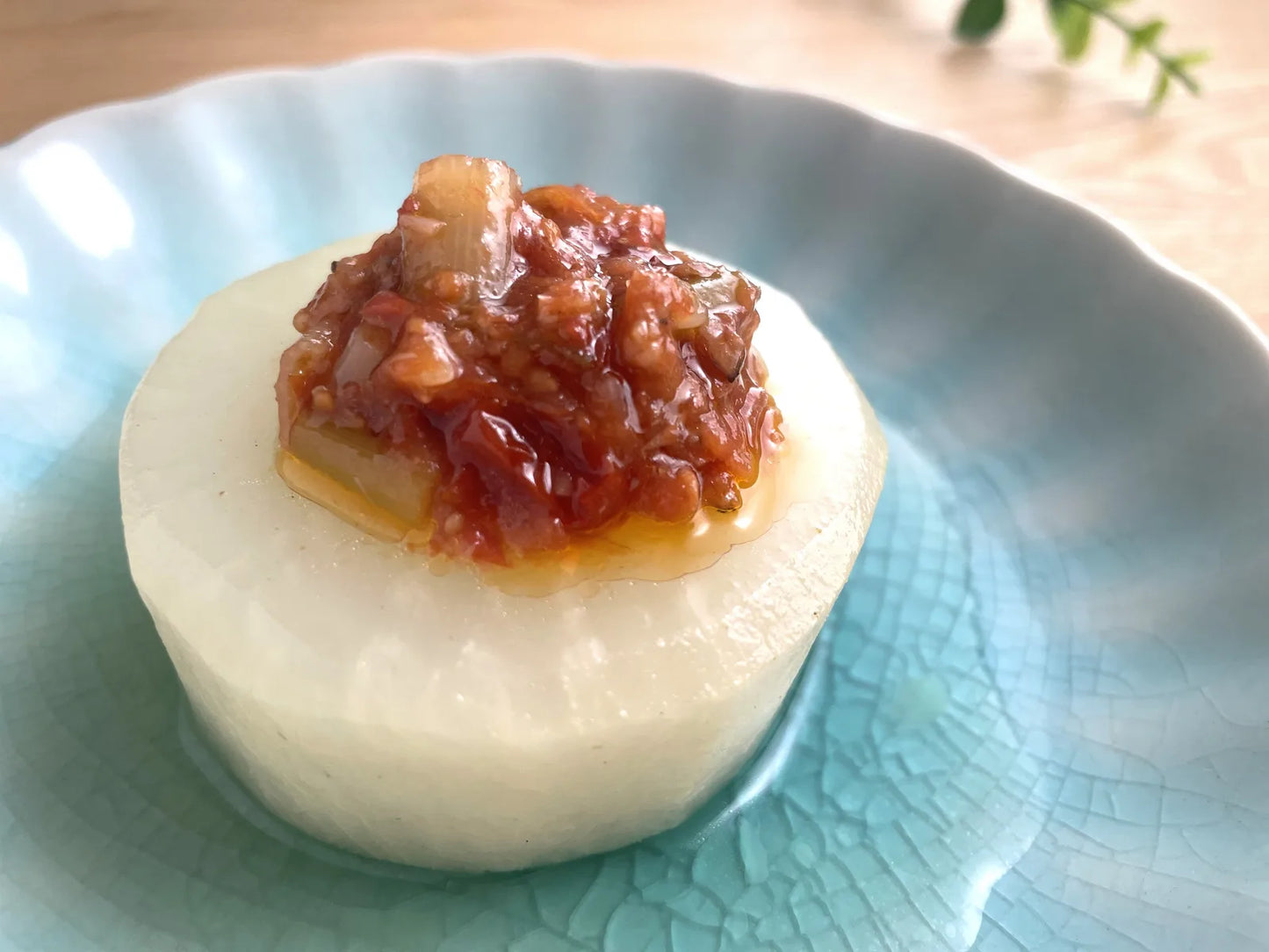 青い和皿に盛った茂で大根の上に、完熟ミニトマトの食べるだしだれをたっぷりのせた料理写真。だしだれの油が皿にとろりと広がる