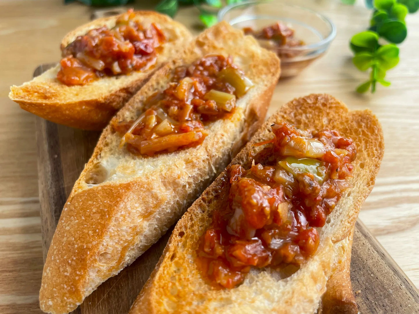 トーストしたバゲット3切れに完熟ミニトマトの食べるだしだれをたっぷりのせたブルスケッタ風の写真。奥に小皿とグリーンが写る